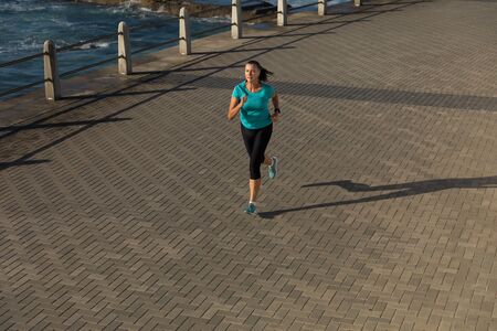 High angle front view of a mature middle aged Caucasian woman working out on a promenade on a sunny...