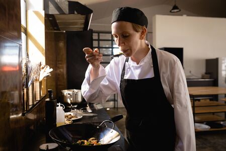 Front view of a Caucasian woman at a cookery class in a restaurant kitchen, blowing hot vegetables...
