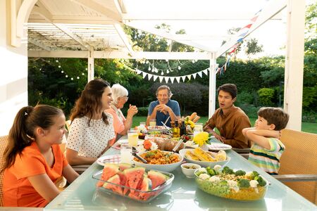Front view of a multi-generation Caucasian family sitting outside at a dinner table set for a meal