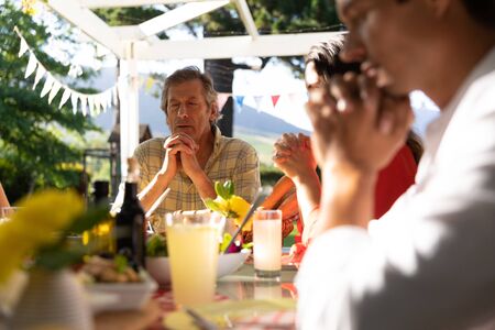 Front view of a Caucasian grandfather and his family sitting outside at a dinner table set for a...