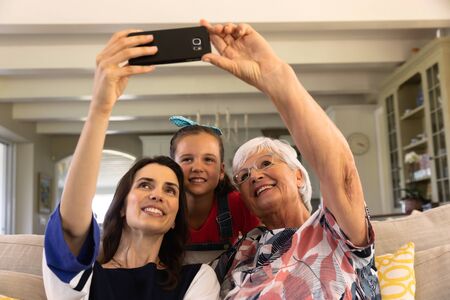 A senior Caucasian woman with her adult daughter and granddaughter on a sofa in the living room