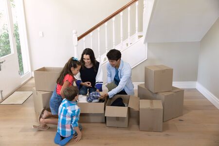 Front view of Caucasian parents with their son and daughter unpacking boxes, sitting on the floor in...
