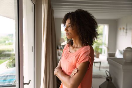 Side view of an African American woman standing in kitchen and looking out of the window.