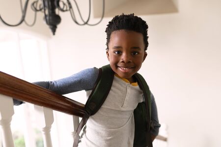 Portrait of smiling African American boy looking to camera with backpack standing on stairs by...