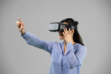 Side view of a Caucasian woman standing wearing a Virtual Reality headset touching a virtual...
