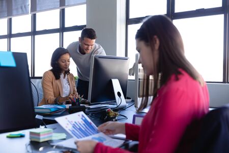 Side view of a Caucasian woman working in a modern office, looking at a chart, with two colleagues working in the background.の写真素材
