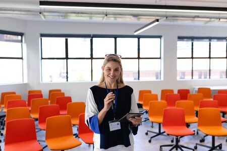 Front view of a Caucasian woman with long blond hair, wearing smart clothes, standing in an empty...