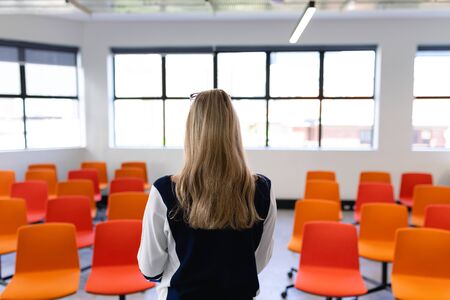Rear view of a Caucasian woman with long blond hair, wearing smart clothes, standing in an empty...