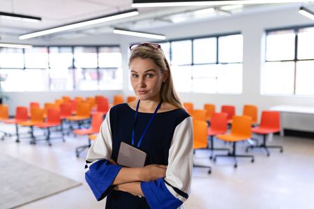 Front view of a Caucasian woman with long blond hair, wearing smart clothes, standing in an empty...