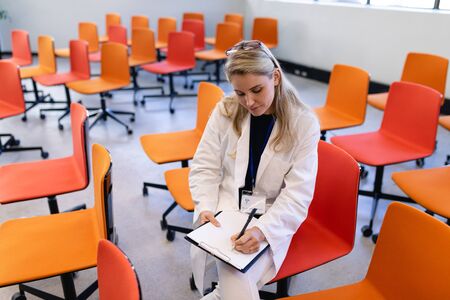 Front view of a Caucasian woman with long blond hair, wearing smart clothes, sitting on a chair in...