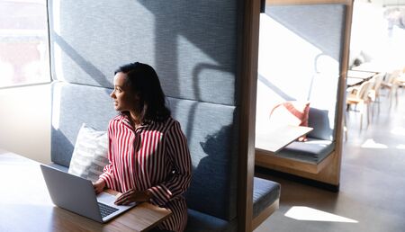 Front view of a mixed race businesswoman working in a modern office, sitting by a desk and using a laptop computer. Social distancing and self isolation in quarantine lockdownの写真素材