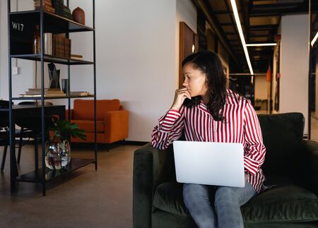 Front view of a mixed race businesswoman working in a modern office, sitting on the armchair and...
