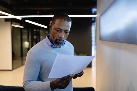Side view of an African American businessman working in the modern office, standing by the armchair...