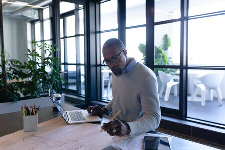 Side view of an African American businessman working in the modern office, sitting by a desk, using...