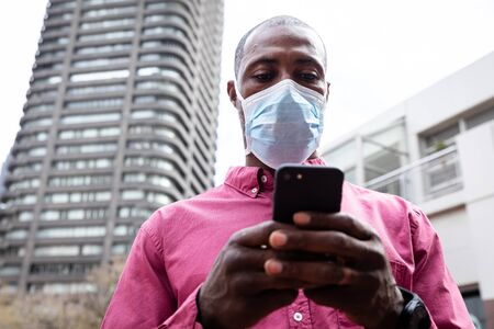 African American man out and about in the city streets during the day, wearing a face mask against...