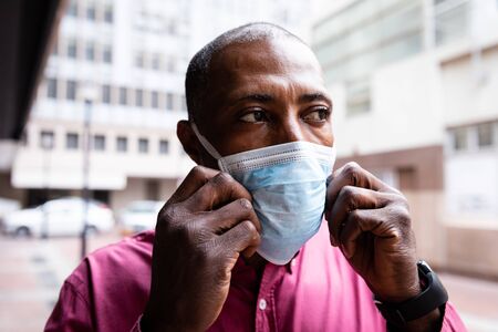 African American man out and about in the city streets during the day, putting on a face masks against air pollution and covid19 coronavirus.の写真素材