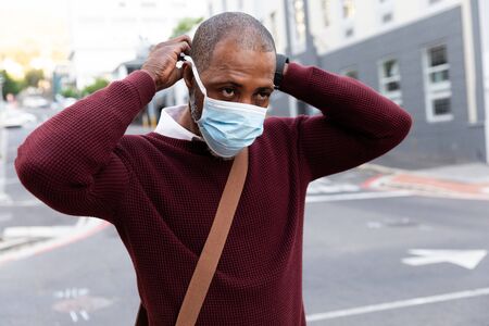 African American man wearing red pullover, out and about in the city streets during the day, putting...
