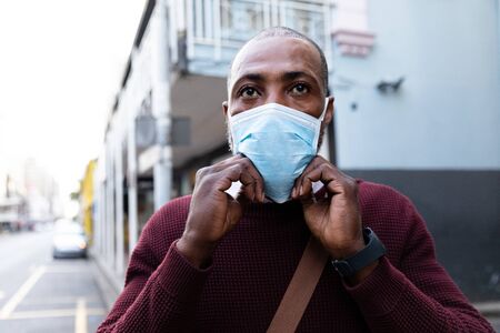 African American man wearing red pullover, out and about in the city streets during the day, putting on a face mask against air pollution and covid19 coronavirus.の写真素材