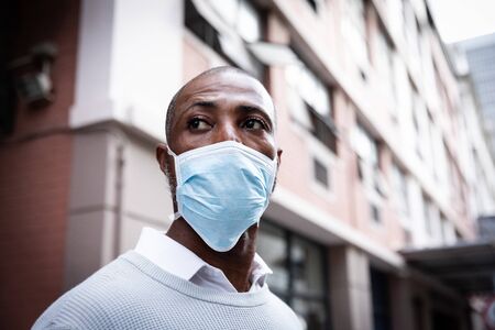 African American man out and about in the city streets during the day, wearing a face masks against air pollution and covid19 coronavirus.の写真素材