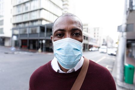 Portrait close up of an African American man out and about in the city streets during the day, wearing a face mask against air pollution and covid19 coronavirus, looking straight into a camera.の写真素材
