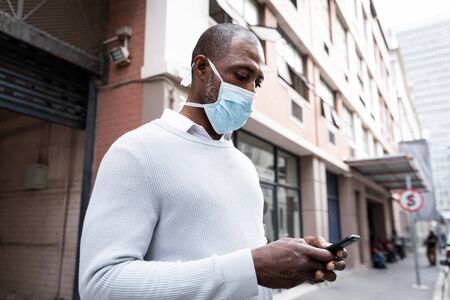 African American man out and about in the city streets during the day, wearing a face mask against...