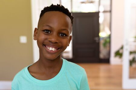 Portrait of a mixed race boy enjoying his time at home, looking at the camera, standing in a...