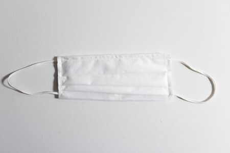 High angle view close up of a face mask protection against pandemic covid 19 coronavirus for safety lying on a white tableの写真素材