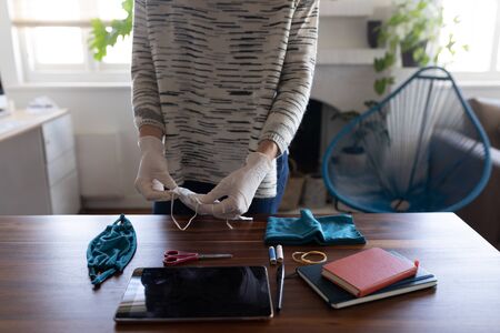 Mid section of Caucasian woman spending time at home self isolating and social distancing in quarantine lockdown during coronavirus covid 19 epidemic, wearing gloves and making a face maskの写真素材