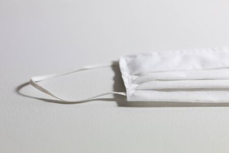 Close up of a white face mask protection against pandemic covid 19 coronavirus and for safety, lying on a white tableの写真素材