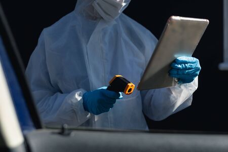 Mid section of Caucasian woman, wearing lab overalls, a face mask and gloves standing outside by a...