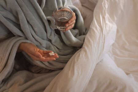 Mid section of sick Caucasian woman at home self isolating and social distancing in quarantine lockdown during coronavirus covid 19 epidemic, taking tabletsの写真素材