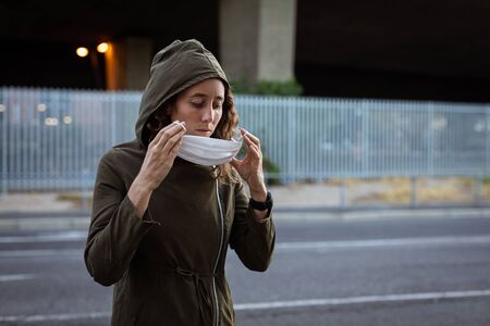 Caucasian woman out and about in the city streets during the day, wearing a hoodie, putting on a...