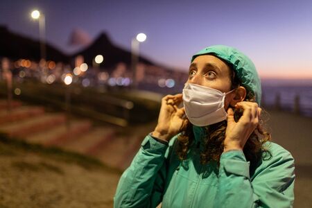 Caucasian woman out and about in the city streets in the evening, wearing a hooded jacket and a face...