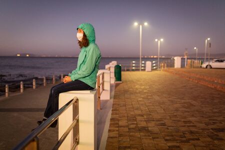 Caucasian woman out and about in the city streets in the evening, wearing a hooded jacket and a face...