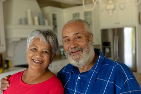 Self isolation in quarantine lock down. portrait close up of a senior mixed race couple at home in their luxury kitchen embracing and smiling to cameraの写真素材