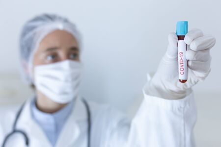 Caucasian female healthcare worker wearing a lab coat, face mask and surgical gloves against...