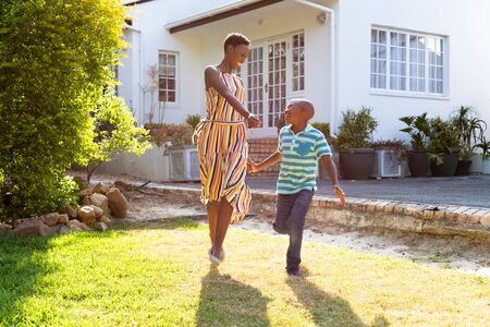 African American woman and her son, spending time together in their garden, jumping on a lawn. Social distancing and self isolation in quarantine lockdown.の写真素材