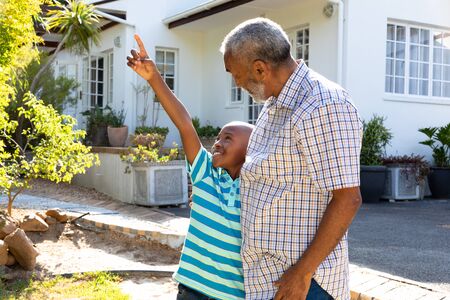Senior African American man and his grandson spending time together in their garden on a sunny day, smiling and embracing.の写真素材