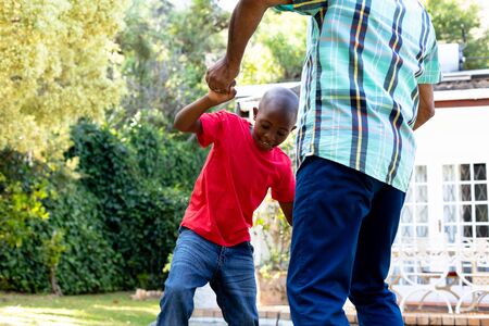Senior African American man spending time with his grandson in their garden on a sunny day, teaching him dancing on the lawn.の写真素材