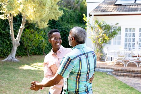 Senior African American couple spending time in their garden on a sunny day, dancing on a lawn. Social distancing and self isolation in quarantine lockdown.の写真素材