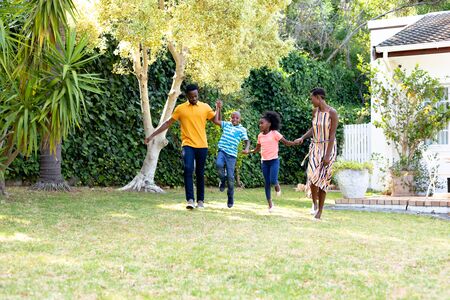 African American man and woman spending time with their son and daughter in their garden, playing on a lawn. Social distancing and self isolation in quarantine lockdown.の写真素材