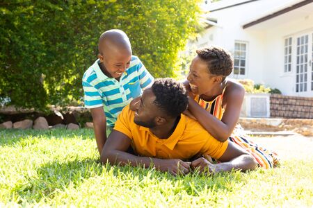 African American woman spending time with her partner and their son, lying on a lawn in the garden. Social distancing and self isolation in quarantine lockdown.