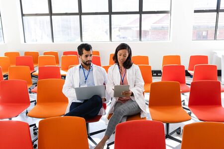 Front view of a Caucasian male and mixed race female medical professionals wearing lab coats,...