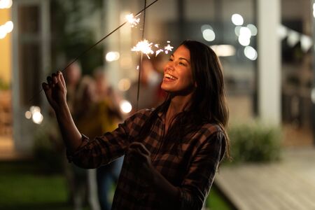 Caucasian woman enjoying her time at the garden, holding sparklers, looking at them and smiling,...