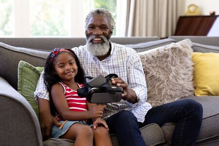 Senior African American man and his granddaughter enjoying their time at home together, sitting on a...