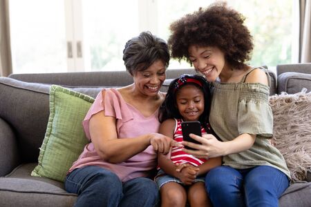 Multi-generation mixed-race family enjoying their time at home together, sitting on a couch,...