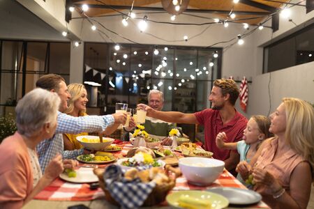 Multi-generation Caucasian family enjoying their time at home together, sitting by a table, talking, looking at each other and smiling, making a toastの写真素材