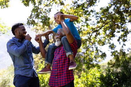 Multi-generation mixed race family enjoying their time at a garden, a mixed race boy is sitting on...