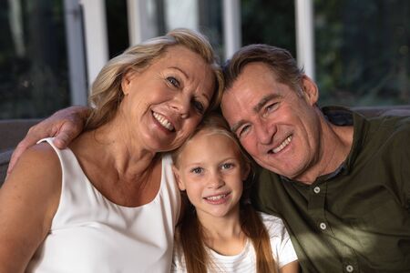 Portrait of a Caucasian girl and her grandparents enjoying her time in a house, sitting on a couch,...