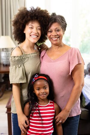 Multi-generation mixed-race family enjoying their time at home together, standing by a couch,...